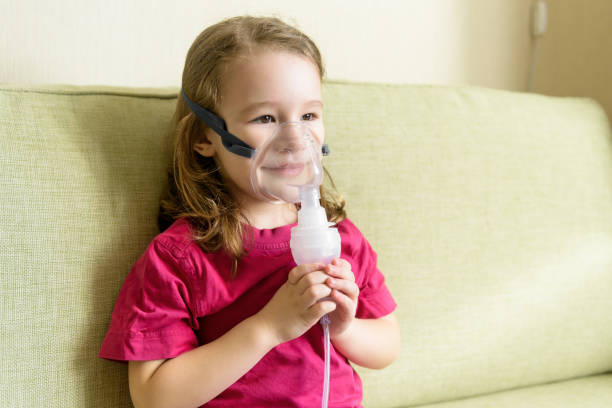 Little girl using inhaler mask at home Little girl holds inhaler mask at home. Sick kid breathes through a nebulizer. Baby using equipment to treat asthma or bronchitis. Concept of treatment of children's respiratory and lung diseases. pediatric nebulizer mask stock pictures, royalty-free photos & images