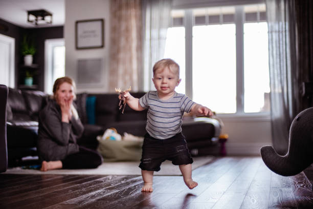 Parents Watching and Helping Baby Son Take First Steps At Home Son practice his first step with his mom. Horizontal and color photo was taken in Quebec Canada. first steps stock pictures, royalty-free photos & images