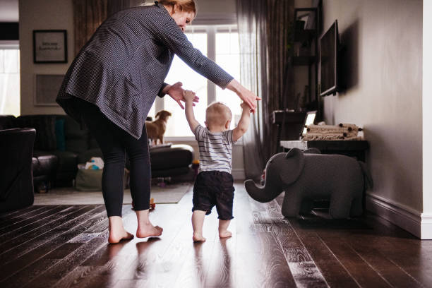 Parents Watching and Helping Baby Son Take First Steps At Home