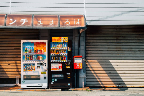 Shari District, Japan - June 3, 2023: Outside a bus station with a red beverage vending machine in Utoronishi near Shiretoko. A passenger waits with his luggage in the background. Spring morning with overcast skies.
