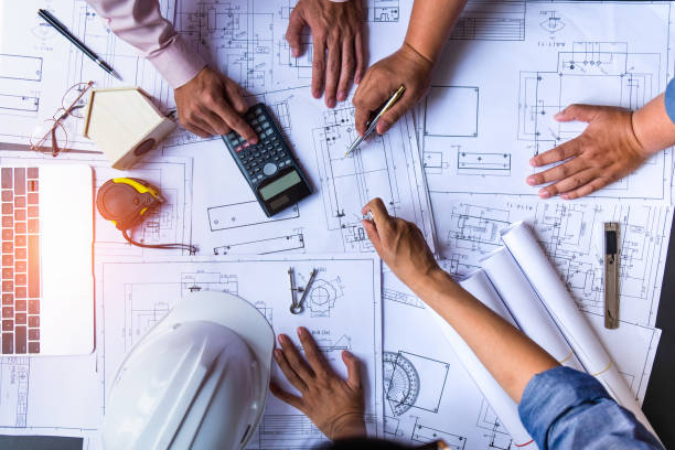 istock engineers pointing to building on blueprint and using laptop to drawing design building Project in office, construction concept. Engineer concept 1145542006
