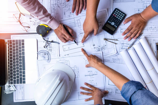 istock engineers pointing to building on blueprint and using laptop to drawing design building Project in office, construction concept. Engineer concept 1145542527