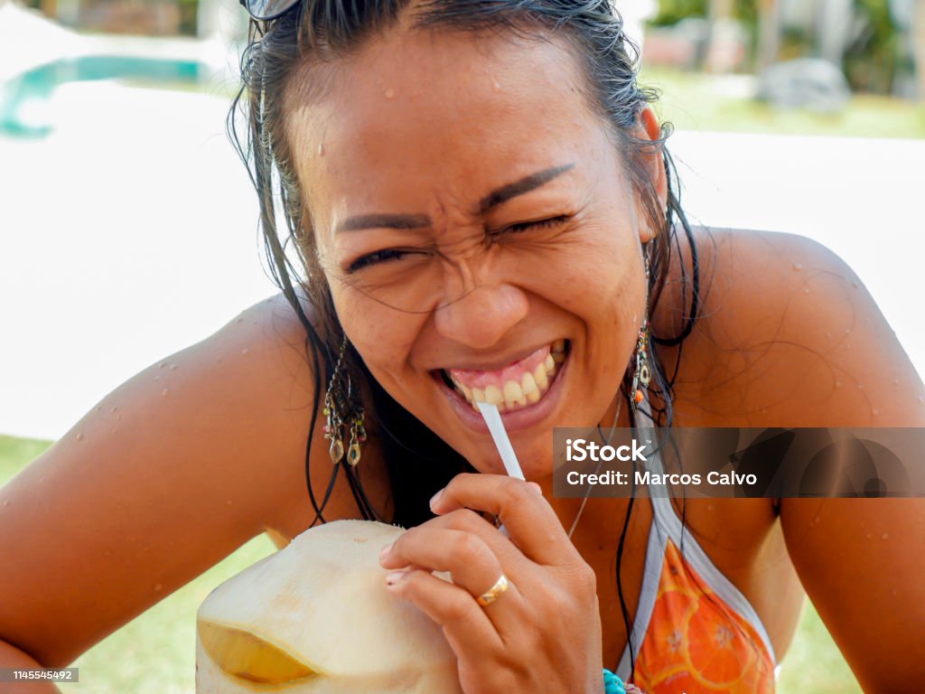 lifestyle natural portrait of 30s or 40s happy and attractive Asian Indonesian woman in bikini drinking coconut water at tropical resort swimming pool smiling cheerful and relaxed enjoying holidays 30-39 Years Stock Photo