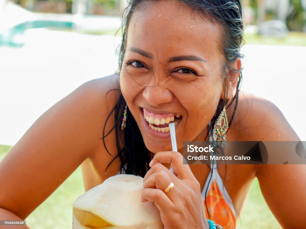 lifestyle natural portrait of 30s or 40s happy and attractive Asian Indonesian woman in bikini drinking coconut water at tropical resort swimming pool smiling cheerful and relaxed enjoying holidays 30-39 Years Stock Photo