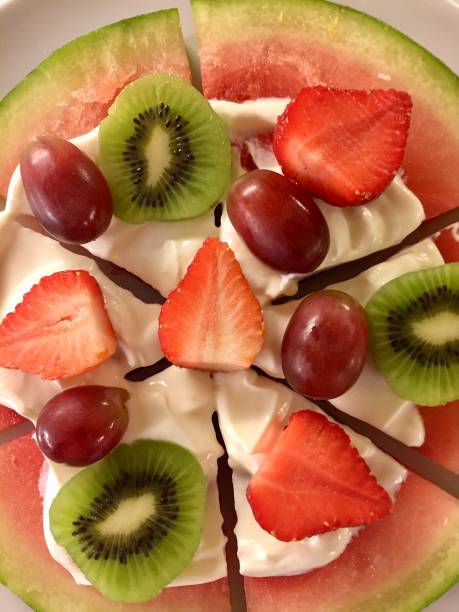 obrázek zdravého pizza dezertu vyrobeného z plátku melounu, krémového řeckého jogurtu, jahod, kiwi ovoce a červených hroznů, foto pudink z ovocné pizzy - šlehačka fotky - stock snímky, obrázky a fotky