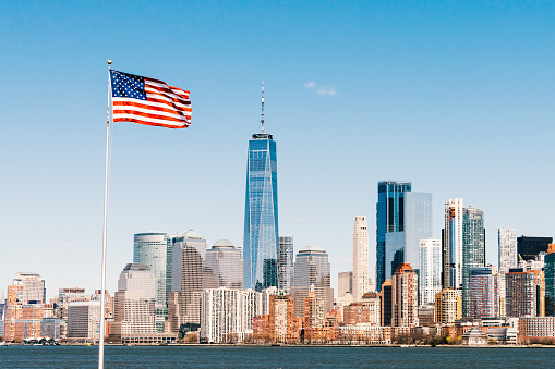 Bandera nacional americana en el día soleado con la ciudad de Nueva York Manhattan isla en el fondo. Paisaje urbano de América, o concepto de símbolo de nación de Estados Unidos photo