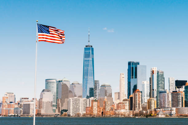 bandera nacional americana en el día soleado con la ciudad de nueva york manhattan isla en el fondo. paisaje urbano de américa, o concepto de símbolo de nación de estados unidos - urbanscape fotografías e imágenes de stock
