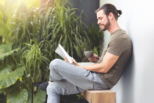 Relaxing Hipster man holding cup of coffee and reading a book at outdoor on his Vacations.