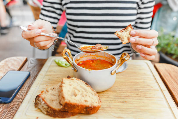 в ресторане под открытым небом женщина ест традиционный венгерский гуляш или томатный суп из кастрюли - hungarian culture стоковые фото и изображения