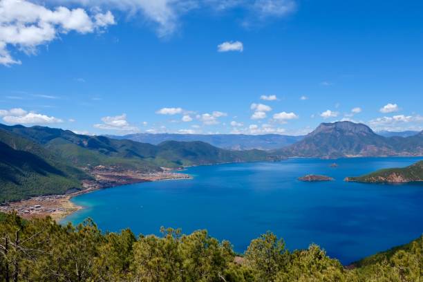 istock deep blue lake surrounded by green mountains. Green trees foreground. Sunny blue sky with white clouds. 1145588515