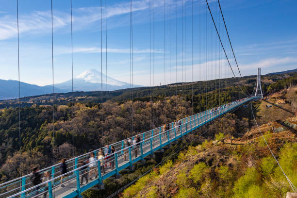 menschen, die auf der brücke mishima skywalk mit dem berg fuji spazieren, der am fernen, klaren, sonnigen tag gesehen wird - erhöhter fußgängerweg stock-fotos und bilder