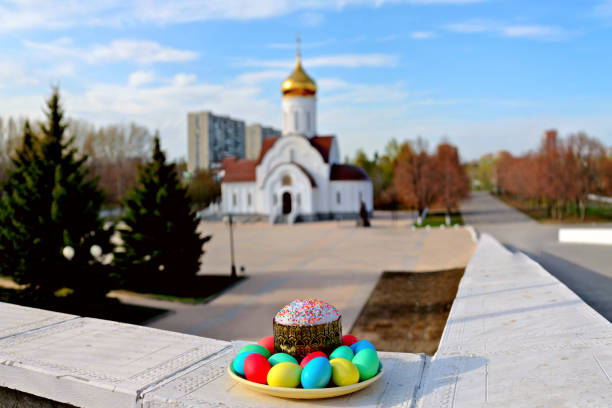 Painted Easter eggs and a cake lie on a plate against a blurred background of the wedding church of Peter and Fevronia of Murom in the city of Togliatti.