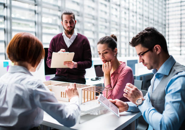 istock Group of young architects with model of a house working in office, talking. 1145610232