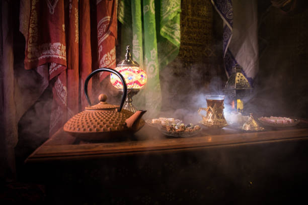 istock Arabian tea in glass with eastern snacks on vintage wooden surface. Eastern tea concept. Low light lounge interior with carpet. Empty space. 1145612478