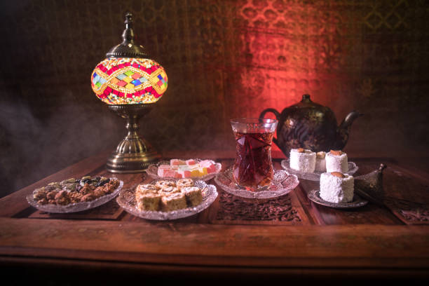 istock Arabian tea in glass with eastern snacks on vintage wooden surface. Eastern tea concept. Low light lounge interior with carpet. Empty space. 1145612491