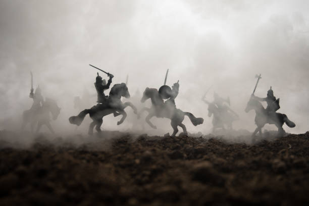 istock Medieval battle scene with cavalry and infantry. Silhouettes of figures as separate objects, fight between warriors on sunset foggy background. Selective focus 1145618691