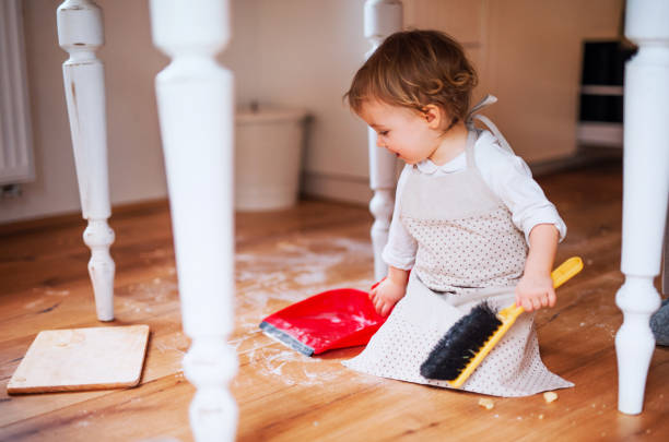 A small toddler girl with brush and dustpan sweeping floor in the kitchen at home. A small toddler girl with brush and dustpan sweeping messy floor in the kitchen at home. flour mess stock pictures, royalty-free photos & images