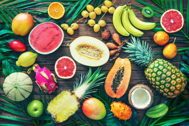 assortimento di frutti tropicali con foglie di palme e piante esotiche su sfondo di legno scuro - healthy eating multi colored orange above foto e immagini stock