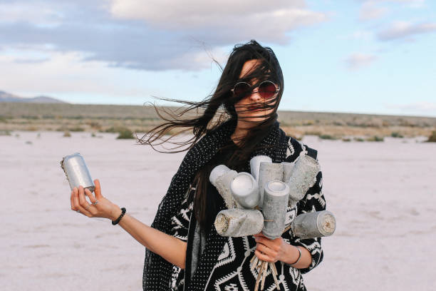 Young woman collecting the thrash cans by the Salton Sea - lake in Southern California, near Coachella Valley. Nature preservation, recycling concepts, presented by a modern, hippie-boho young woman.
