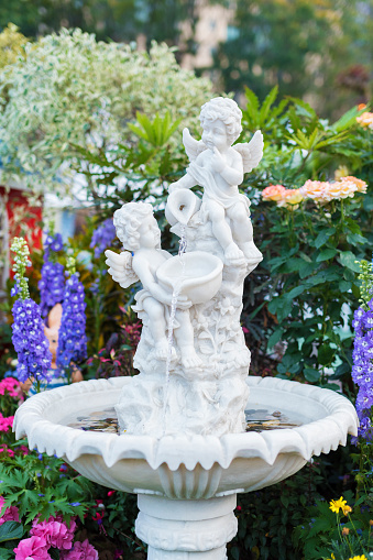 Fountain and sculpture of cherub in backyard flower garden