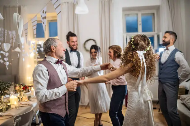 Photo of A young bride dancing with grandfather and other guests on a wedding reception.