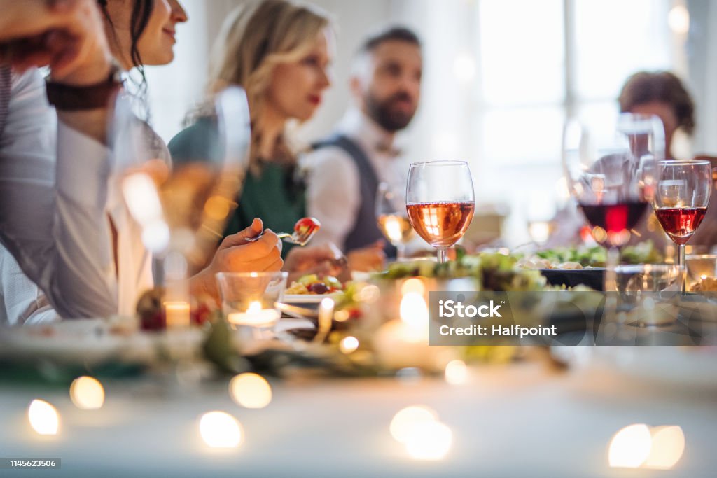 Una grande famiglia seduta a un tavolo ad una festa di compleanno al coperto, che mangia. - Foto stock royalty-free di Cena