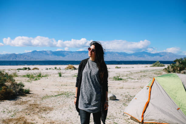 Camping in tent by Salton Sea in California Young woman camping in tent by the Salton Sea - lake in Southern California, near Coachella Valley. She is wearing modern, laid back clothing, enjoying the morning sun. coachella people stock pictures, royalty-free photos & images