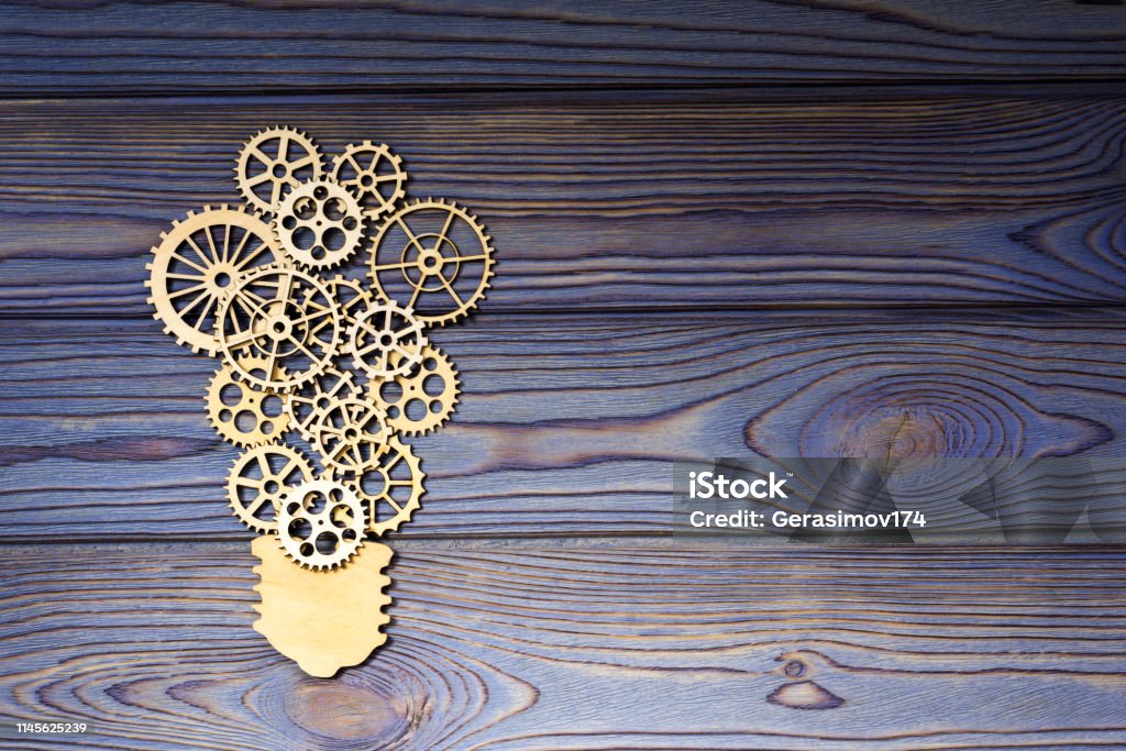 Wooden gears in the form of a light bulb on a wooden background. Wooden gears in the form of a light bulb on a wooden background. the concept of the mechanism of the business idea. Gear - Mechanism Stock Photo