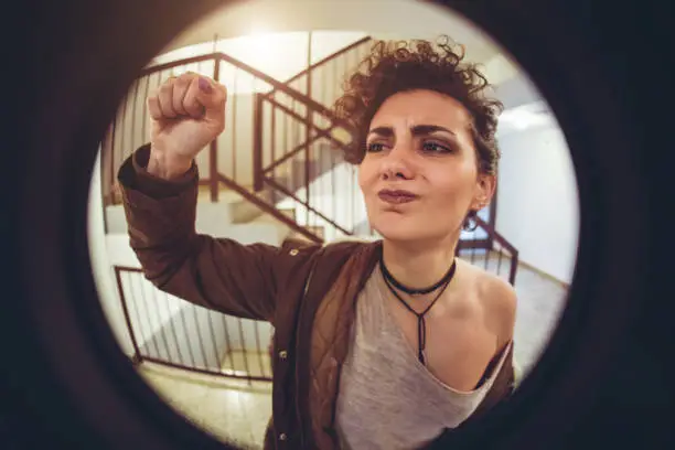 Young, angry, woman knocking on the door, seen through spy hole.