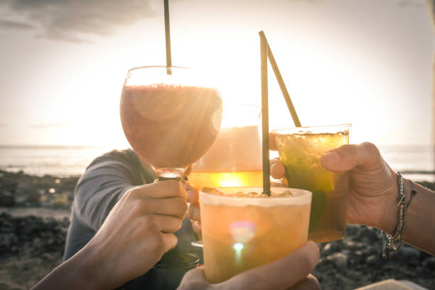 greetings to best friends, group of friends enjoying evening drinks at the beach at sunset. concept of vacation, carefree, end-of-day relaxation, celebration and well-being. - day to sunset imagens e fotografias de stock