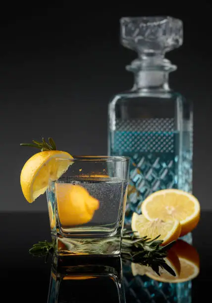 Gin-tonic with lemon slices and twigs of rosemary on a black reflective background.