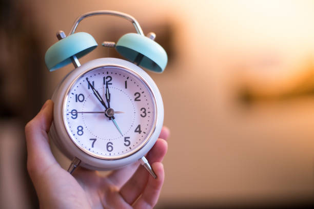 istock Man is holding an alarm clock in the hand, blurry background 1145641222