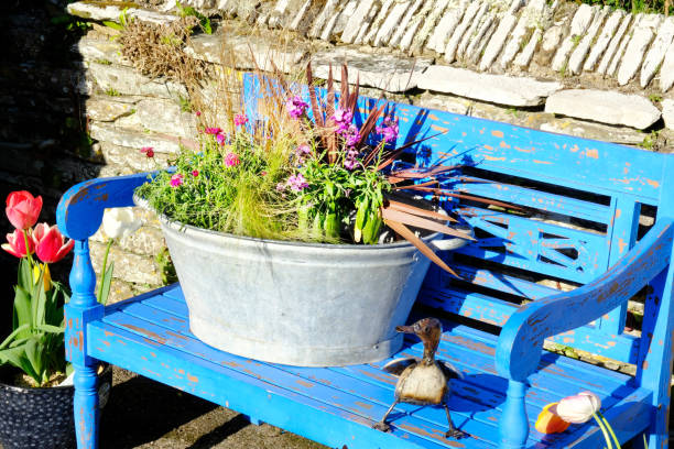 An old-fashioned tin bath used as a planter full of flowering plants resting on a blue bench.