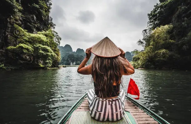 A beautiful Vietnamese woman rides a traditional boat through the mountains and jungle of northern Vietnam