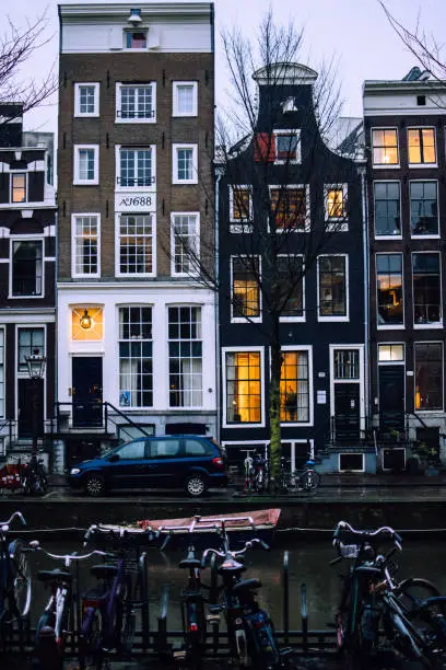 Photo of Traditional bricked Dutch houses in Amsterdam, Netherlands. Cars and bicycles in front of the front walls. Window lights reflected in a canal water