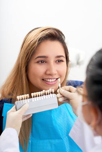 Professional dentist picking perfect shade of white veneers for female patient