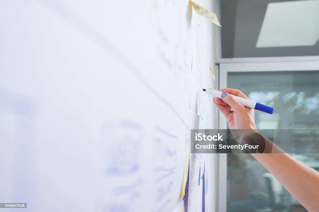 Female entrepreneur drawing on whiteboard Hand of female business executive drawing diagram on office whiteboard with blue marker Whiteboard - Visual Aid Stock Photo