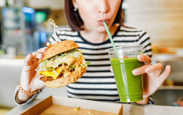 eine junge frau trinkt grüne smoothies und isst einen burger in einem veganen fast-food-restaurant - cooking clothing foods and drinks equipment stock-fotos und bilder