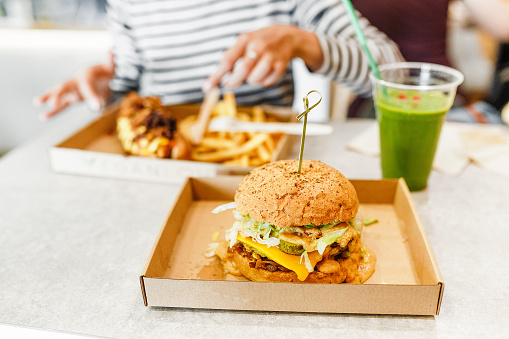 A young woman drinks green smoothies and eats a burger in a vegan fast food restaurant