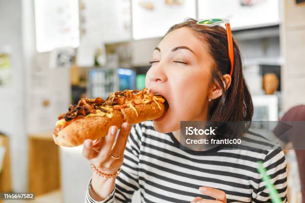 Young Pretty Girl Eating Big Hotdog In Fastfood Restaurant Stock Photo - Download Image Now