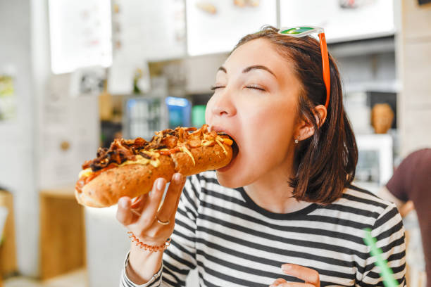 young pretty girl eating big hotdog in fastfood restaurant - burger hamburger large food imagens e fotografias de stock