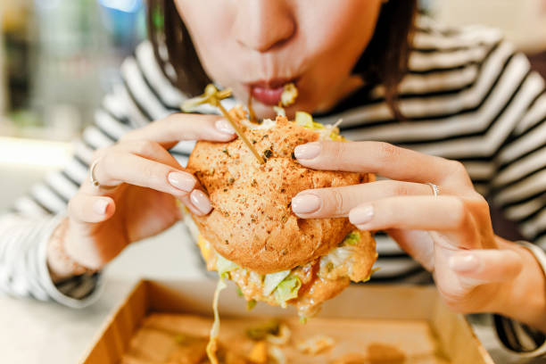 mujer comiendo una hamburguesa en la moderna cafetería fastfood, concepto de almuerzo - comer fotografías e imágenes de stock