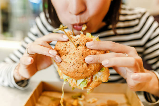 femme mangeant un hamburger dans le café moderne de fastfood, concept de déjeuner - matière grasse aliment photos et images de collection