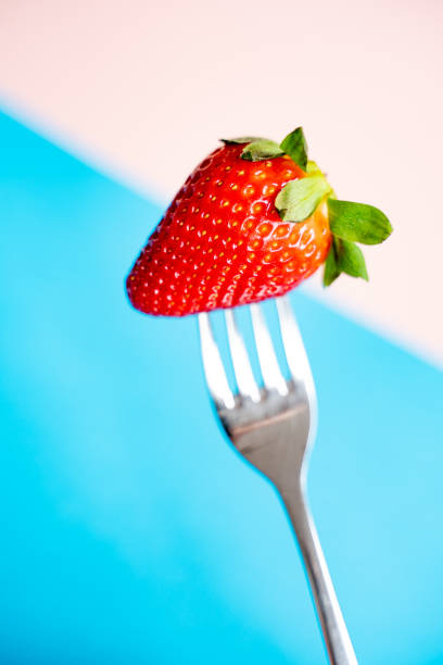 istock Juicy strawberry on a fork against a colored background 1145654408
