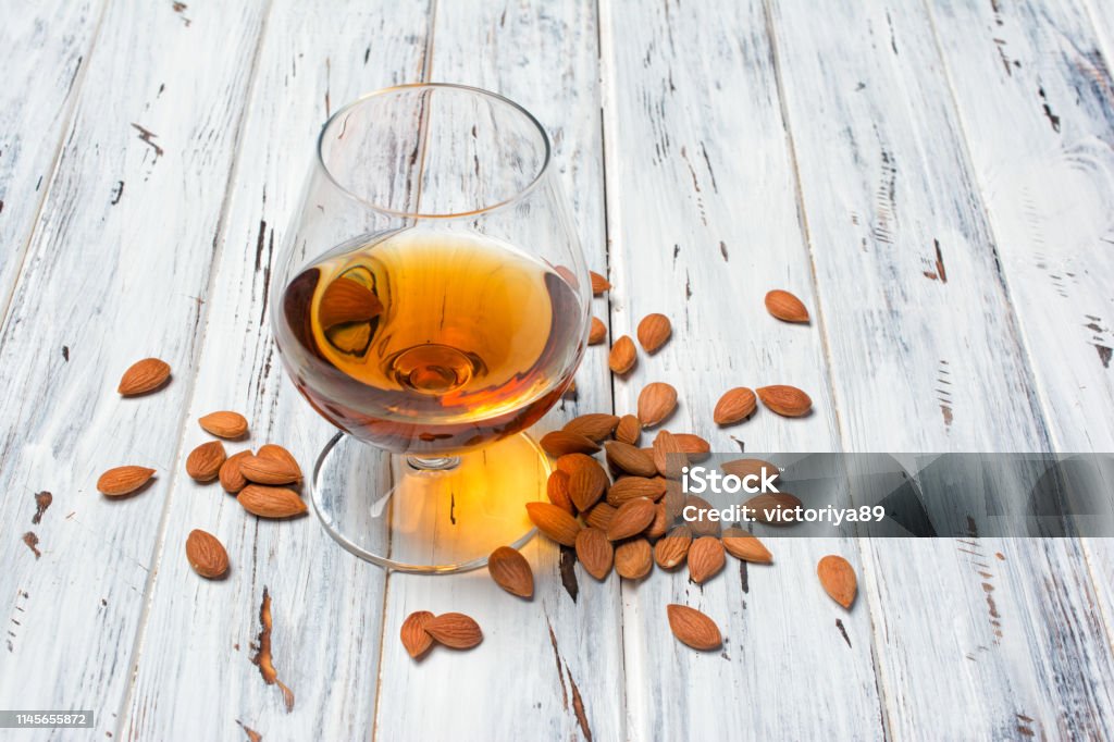 Strong alcoholic beverage amaretto liqueur in sniffer glass Strong alcoholic beverage amaretto liqueur in sniffer glass for tasting on white wooden background with copy space Alcohol - Drink Stock Photo