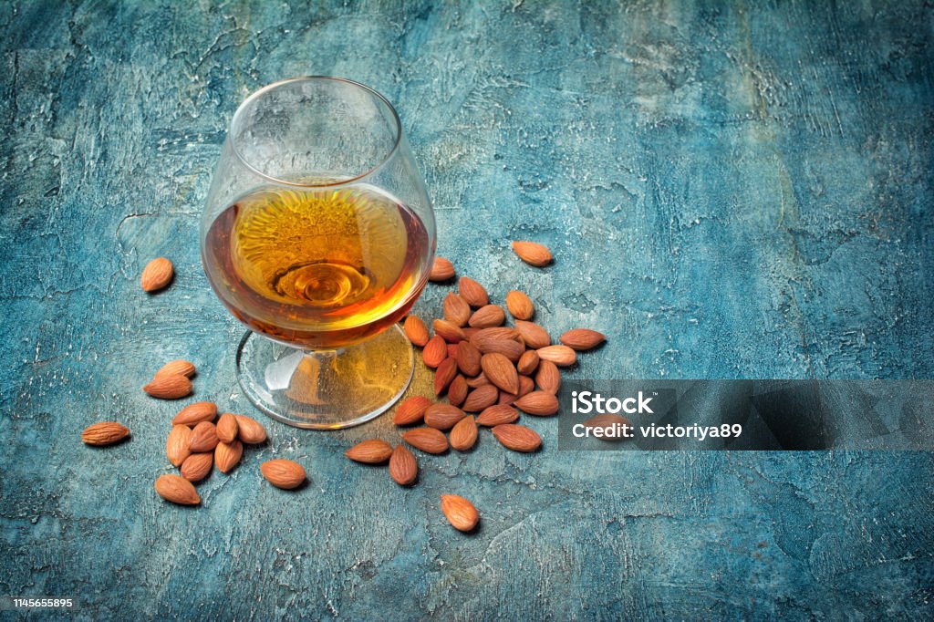 Strong alcoholic beverage amaretto liqueur in sniffer glass Strong alcoholic beverage amaretto liqueur in sniffer glass for tasting on blue concrete background with copy space Nut - Food Stock Photo