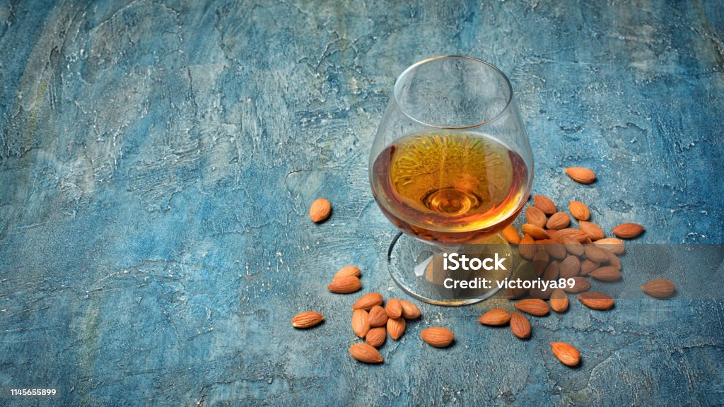 Strong alcoholic beverage amaretto liqueur in sniffer glass Strong alcoholic beverage amaretto liqueur in sniffer glass for tasting on blue concrete background with copy space Alcohol - Drink Stock Photo