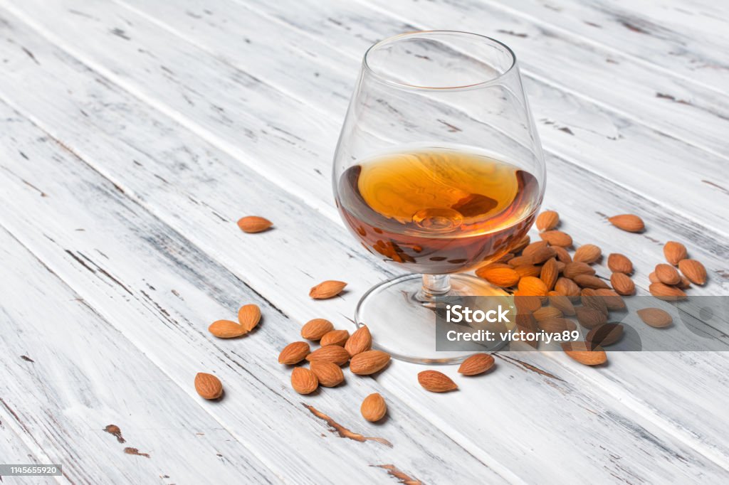 Strong alcoholic beverage amaretto liqueur in sniffer glass Strong alcoholic beverage amaretto liqueur in sniffer glass for tasting on white wooden background with copy space Alcohol - Drink Stock Photo