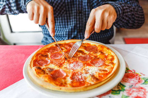 istock Happy hungry man eating pizza using fork and knife in italian restaurant 1145662246