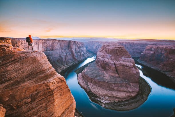 Hiker overlooking Horseshoe Bend at sunset, Arizona, USA A male hiker is standing on steep cliffs enjoying the beautiful view of Colorado river flowing at famous Horseshoe Bend overlook in beautiful post sunset twilight on a summer evening, Arizona, USA horseshoe bend river stock pictures, royalty-free photos & images